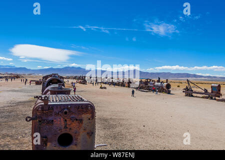 Train cemetery, Uyuni, Bolivia : Abandoned old steam locomotives, vintage trains lie on the white ground and some tourist visiting a popular landmark Stock Photo