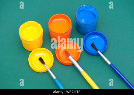 Three paintbrushes and gouaches of different colors: yellow, orange, blue Stock Photo