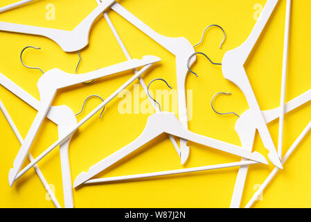 White clothes hangers on yellow background with copy space. Flat lay. Top view. Minimalism style. Creative layout. Fashion, store sale, shopping conce Stock Photo