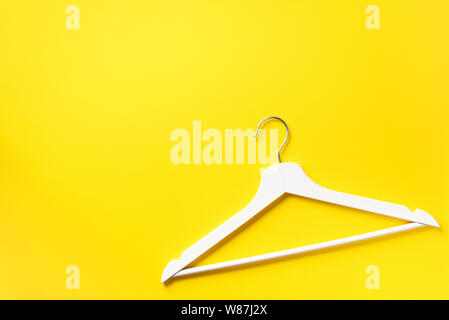 White clothes hangers on yellow background with copy space. Flat lay. Top view. Minimalism style. Creative layout. Fashion, store sale, shopping conce Stock Photo