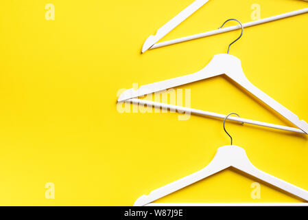 White clothes hangers on yellow background with copy space. Flat lay. Top view. Minimalism style. Creative layout. Fashion, store sale, shopping conce Stock Photo