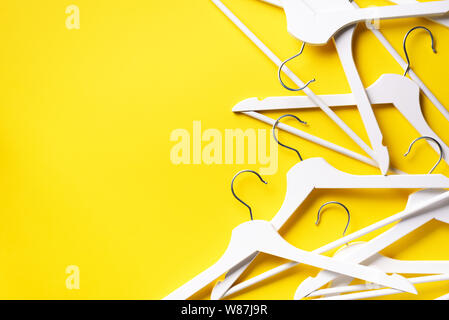 White clothes hangers on yellow background with copy space. Flat lay. Top view. Minimalism style. Creative layout. Fashion, store sale, shopping conce Stock Photo