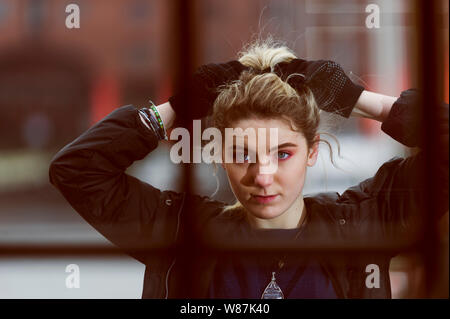Girl looks directly into the camera through leaded windows while fixing her hair. Stock Photo