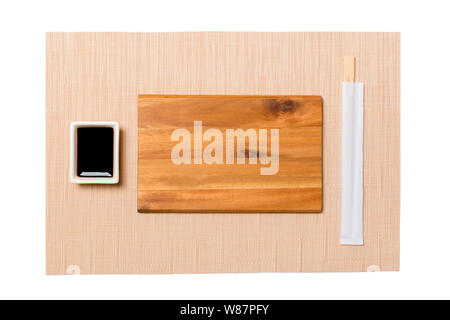 Empty rectangular brown wooden plate with chopsticks for sushi and soy sauce on brown sushi mat background. Top view with copy space for you design. Stock Photo