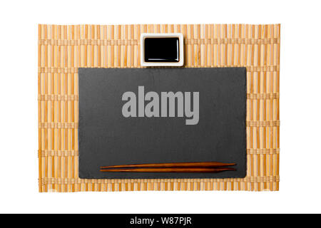 Empty rectangular black slate plate with chopsticks for sushi and soy sauce on yellow bamboo mat background. Top view with copy space for you design. Stock Photo