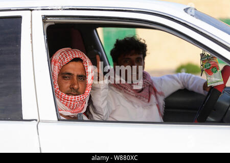 Oman, portrait of two mid-adult men in headdress sitting in car, making hand gesture Stock Photo