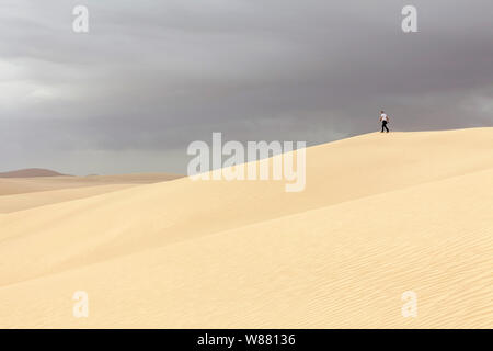 Man walking on sand dunes in desert landscape Stock Photo