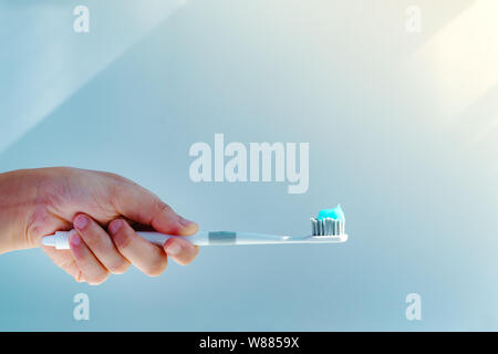Woman hand holding toothbrush with toothpaste applied on. Closeup of  white toothbrush with blue tooth paste Stock Photo
