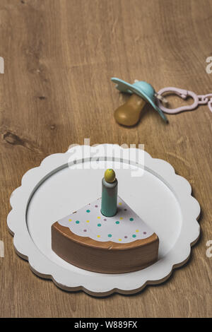 Toy birthday cake piece with one candle and a pacifier over a wooden surface Stock Photo