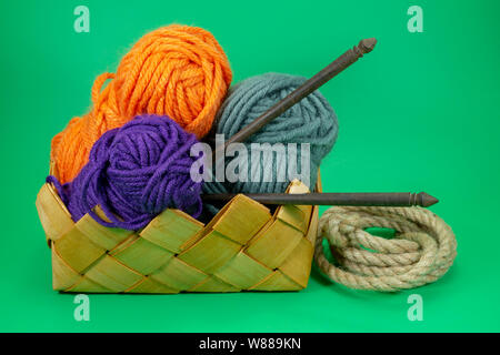 Handicraft and needlework concept - close up of wicker basket with colorful balls of yarn, jute rope and knitting needles on green background with fre Stock Photo