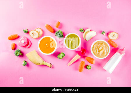 Infant baby food concept. Bowls with vegetable fruit puree, green, orange, yellow colors - broccoli, carrots, banana, apple. With baby accessories and Stock Photo