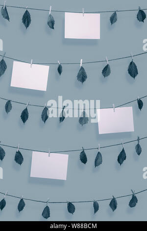 Blank paper notes and dried leaves hanging on clotheslines with wooden clips. Paper sheet frames in blue monochrome color. Environment concept. Nature Stock Photo