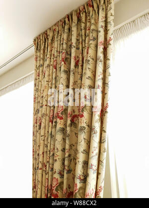 Vintage beige curtains hanging on window with colorful pattern in a light room Stock Photo