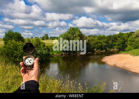 Hand holds the compass against the backdrop of the river Stock Photo