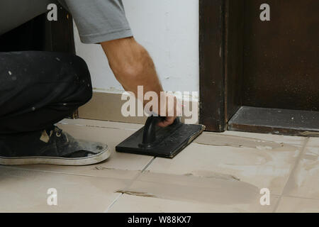 Worker putting fugue on the wall in bathroom. Grouting ceramic tiles, close up Stock Photo