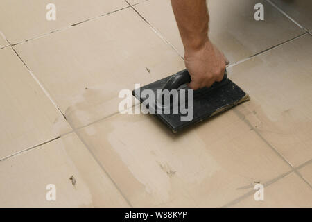 Worker putting fugue on tiles on the floor in corridor. Grouting ceramic tiles, close up Stock Photo