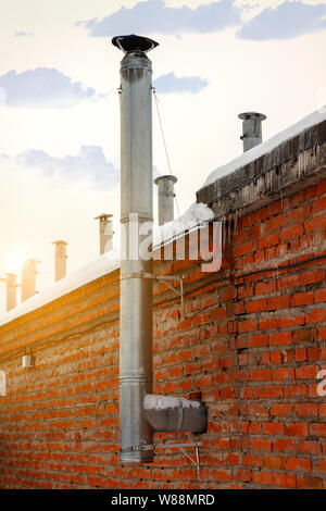 Large metal chimney against the sky and brick wall. Stock Photo