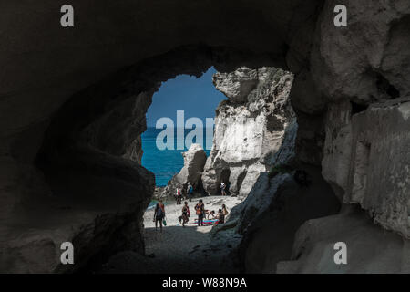 A beautiful beach accesible by a tunnel in a rock with some people. Sicily, Italy. Stock Photo