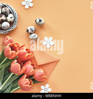 Easter flat lay on orange paper with copy-space. Quail eggs in bird nest, Spring tulips, envelope and flower decorations Stock Photo