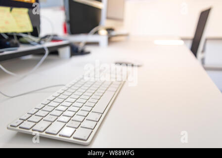 Closeup view of keyboard on white desktop, and blurry background of yellow notepads on desktop computer's monitors and office accessories with white i Stock Photo