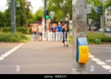 Yellow pedestrian crossing sign or crosswalk push button set up on metal post beside pedestrian crossing on the street in Germany. Stock Photo