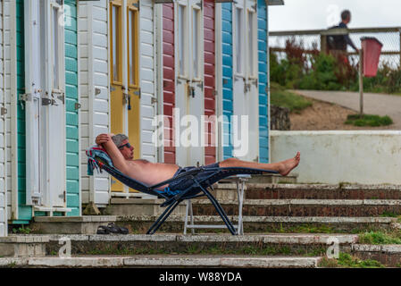 Bude, North Cornwall, England. Thursday 8th August 2019. UK Weather. With impending stormy weather forecast for later today, a holidaymaker enjoys a moment sunbathing as the clouds gather over Bude North Cornwall. Credit: Terry Mathews/Alamy Live News Stock Photo