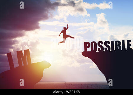 Man jumping over impossible or possible over cliff on sunset background Stock Photo