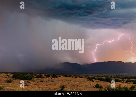 A sunset lightning bolt strikes Mingus Mountain as monsoon thunderstorm with heavy rain moves across the Verde Valley near Cottonwood, Arizona, USA Stock Photo