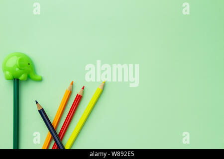 Light green  pencil sharpener in the form of an elephant and five chaotic pencils on a pale green background Stock Photo