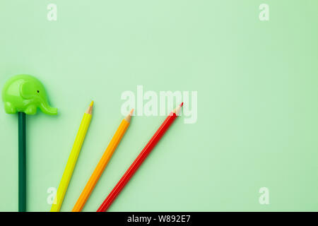 Green pencil sharpener in the form of an elephant and four pencils on a pale green background Stock Photo