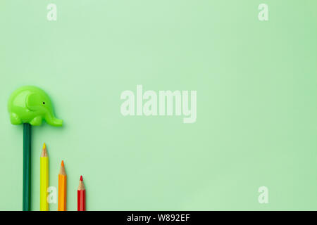 childish pencil sharpener in the form of an elephant and four pencils stairs down on a pale green background Stock Photo