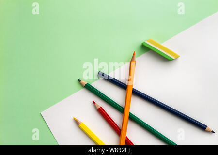 white sheet of paper, five pencils and an eraser on a light green paper background. Copyspace Stock Photo