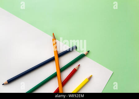 white sheet of paper and five pencils on a pea green color paper background. Copyspace Stock Photo