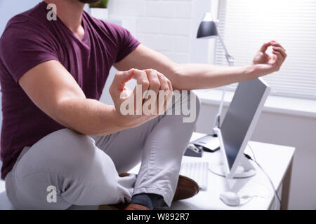 Young Businessman Sitting On Desk Meditating In Office Stock Photo