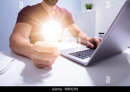 Close-up Of A Businessman's Hand Holding Illuminated Light Bulb In Office Stock Photo