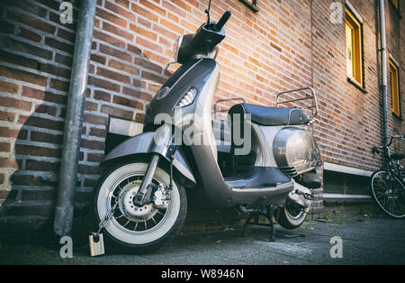 Scooter vintage italian moto. City transportation retro vehicle parked and locked with chain. Rotterdam city center, low angle view Stock Photo