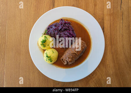 Rinderroulade, Beef roll or roulades, traditional German meal, serve with pickled red cabbage, dumplings potatoes and sauce on white plate . Stock Photo