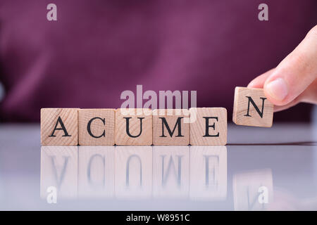 A Person's Hand Placing Last Alphabet Of Word Acumen Over White Reflective Desk Stock Photo