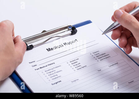 Overhead View Of Human Hand Holding Pen With Medical Report On Clipboard Over White Background Stock Photo
