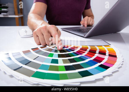 An Architect Designer's Hand Choosing Color From Swatch Over White Desk Using Laptop In Office Stock Photo