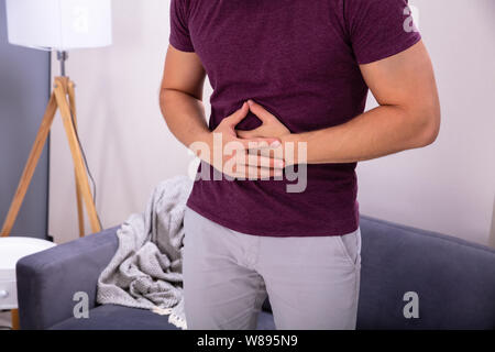 Midsection Of Man Suffering From Stomach Ache Standing Near Sofa Stock Photo