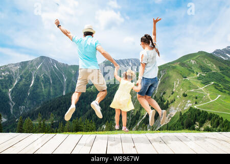 Happy Family With Little Girl Jumping In Austrian Mountains In Summer Stock Photo