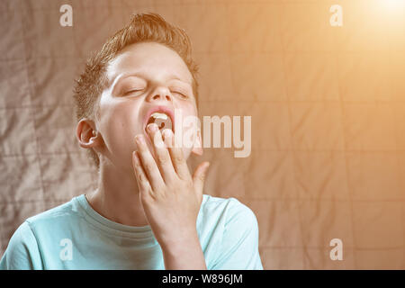 the boy in the blue t-shirt is tired, wants to sleep and yawns Stock Photo