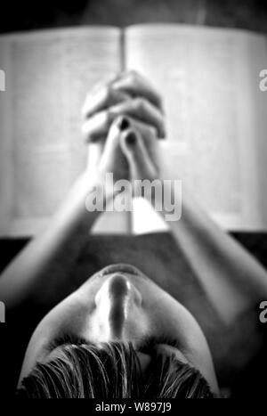 Girl praying with opened book in the background. Stock Photo