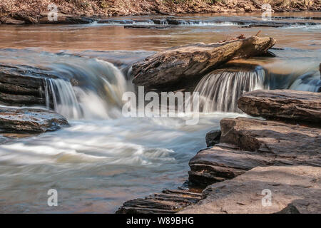 Small waterfalls of water tumbling over rocks downstream in a river on a sunny day in winter up close Stock Photo