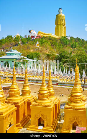 The view through the small gilt stupas of Aung Sakkya Pagoda complex on the giant Reclining and Standing Buddha statues of Maha Bodhi Ta Htaung Monast Stock Photo