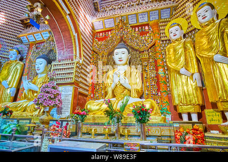 MONYWA, MYANMAR - FEBRUARY 22, 2018: Watch ornate altar of Thanboddhay Pagoda with statues of Standing and Sitting Buddha, decorated with gilt and man Stock Photo