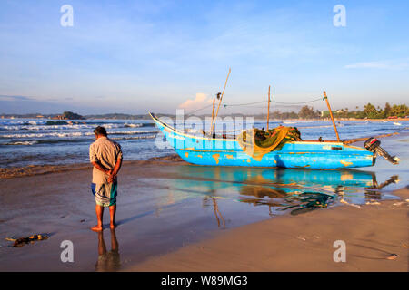 Mirissa, Sri Lanka - Decmber 30th 2016: Man stood by a traditional fishing boat ashore. The boats return early morning after a nights fishing. Stock Photo