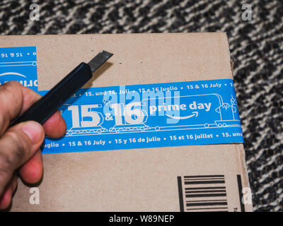 PARIS, FRANCE - JUL 4 2109: Man hand using cutter to unpack new Amazon Prime Day cardboard parcel with special blue scotch tape for the Prime Day Stock Photo