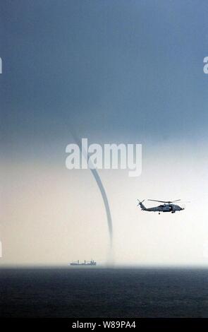 A Navy HH-60H Seahawk helicopter keeps a wary eye on a nearby vessel and a waterspout while patrolling in the South China Sea off the coast of Malaysia on Sept. 5, 2004.  The Seahawk is attached to Helicopter Anti-Submarine Squadron 4 from Naval Station North Island in San Diego, Calif. Stock Photo